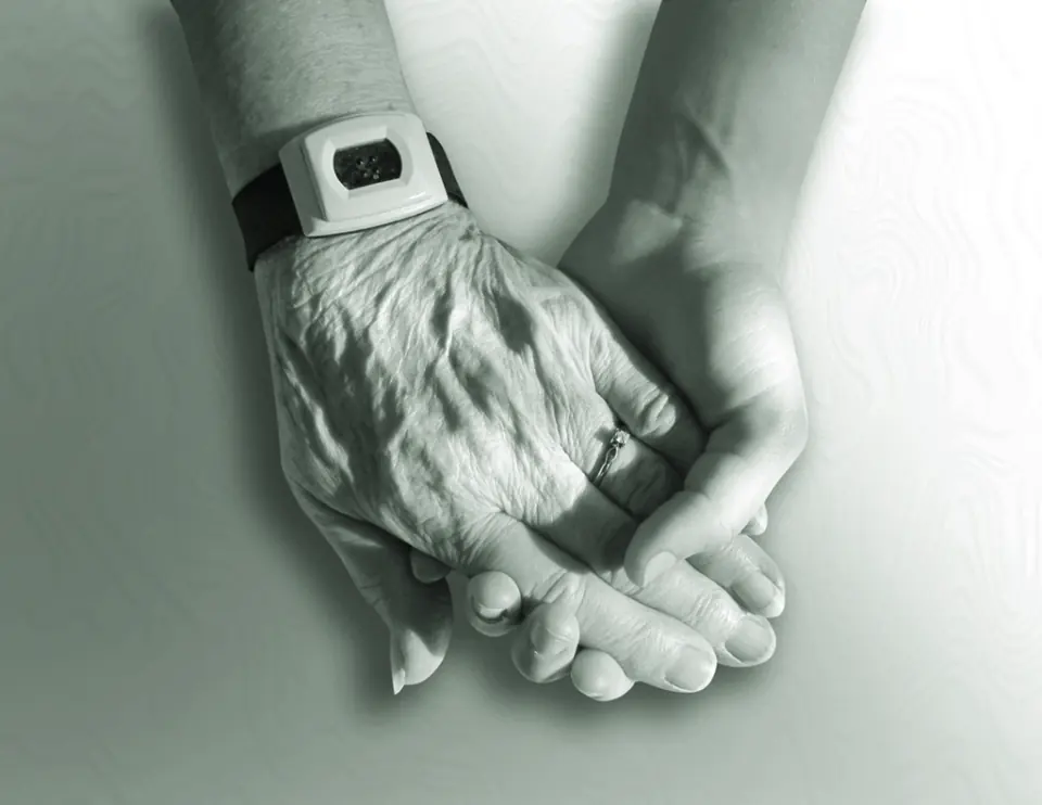 An older person's hand resting in the hands of a supporting carer