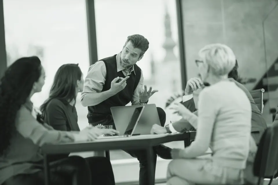 A manager leading a discussion with colleagues around a table in a bright meeting room